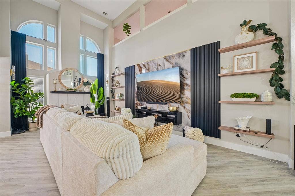Vaulted ceilings with high arched windows, wood-finish flooring, built-in shelving, and a media wall with stone-finish and paneled accents