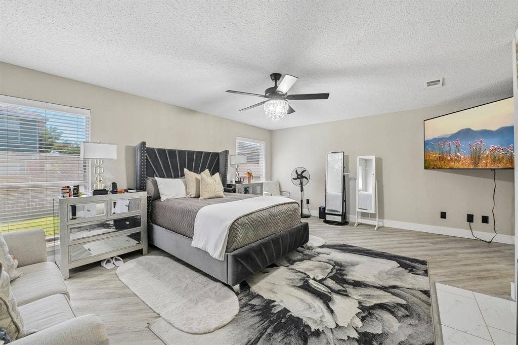 Spacious room featuring light-toned wood-finish flooring, a contemporary ceiling fan with a chandelier light fixture, and multiple windows with blinds