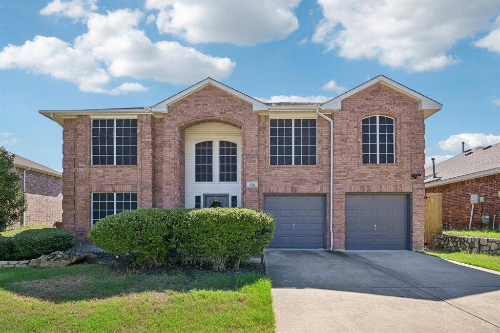 Two-story brick exterior with a prominent arched entry, dual garage doors, and multiple multi-pane windows
