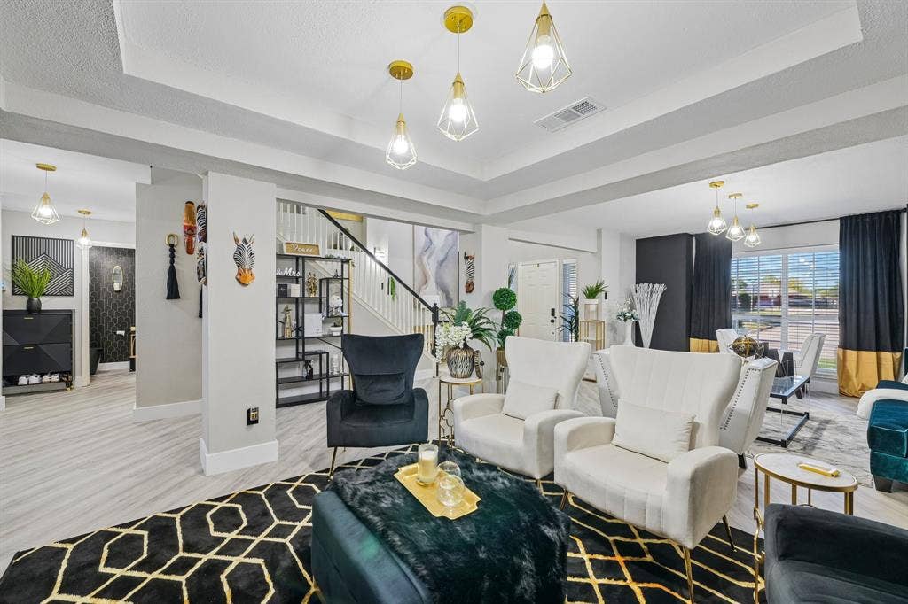 Recessed lighting, wood-finish flooring, staircase with dark handrail, tray ceiling, and modern pendant light fixtures