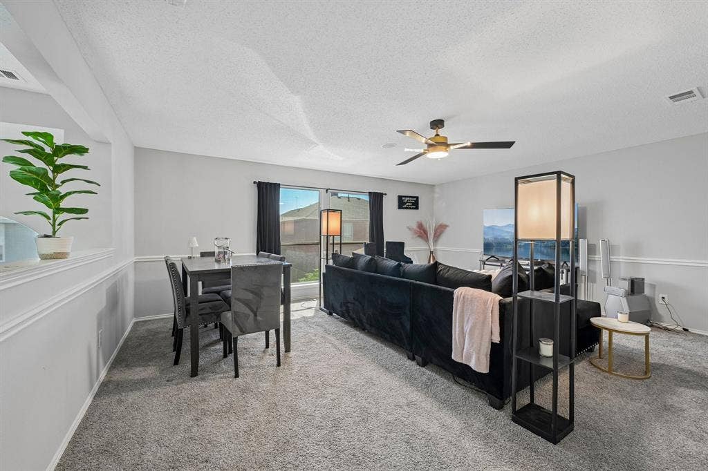 Open-concept living space featuring light gray walls, carpet flooring, a ceiling fan, and sliding glass doors