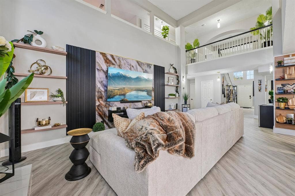 Two-story living area with high ceilings, wood-finish flooring, a decorative accent wall, and built-in shelving