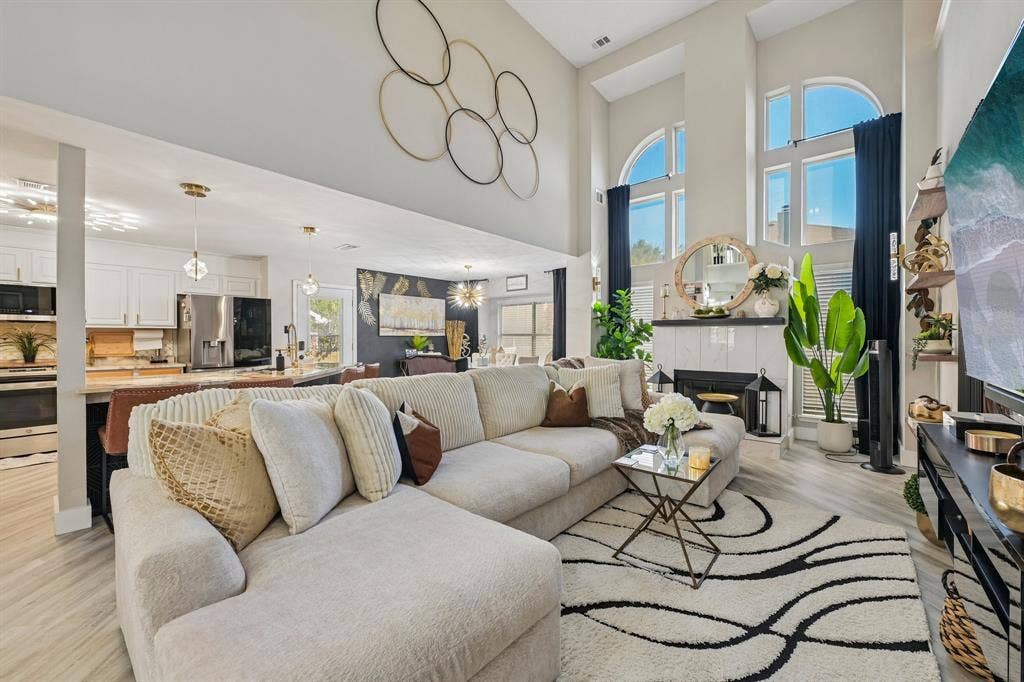Two-story living area featuring tall arched windows, a fireplace with a white tile surround, and light wood-finish flooring