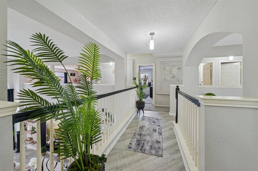 Upper-level hallway with wood-finish flooring, white railing with dark top, and arched architectural detail