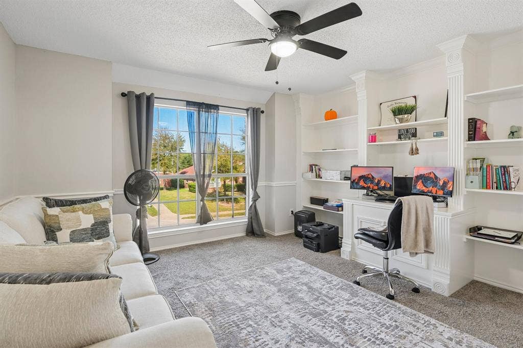Built-in shelving, large window, ceiling fan with integrated lighting, carpet flooring