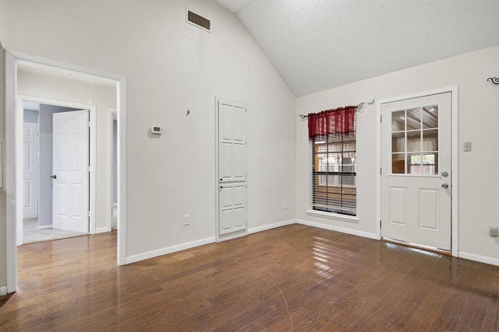 Vaulted ceiling, wood-finish flooring, built-in storage cabinet, window with blinds, and exterior access door with glass panels