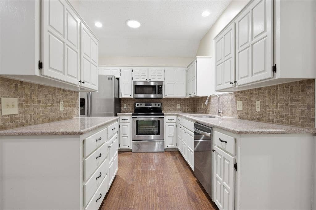 White cabinetry, stainless steel appliances, mosaic tile backsplash, speckled countertops, and wood-finish flooring