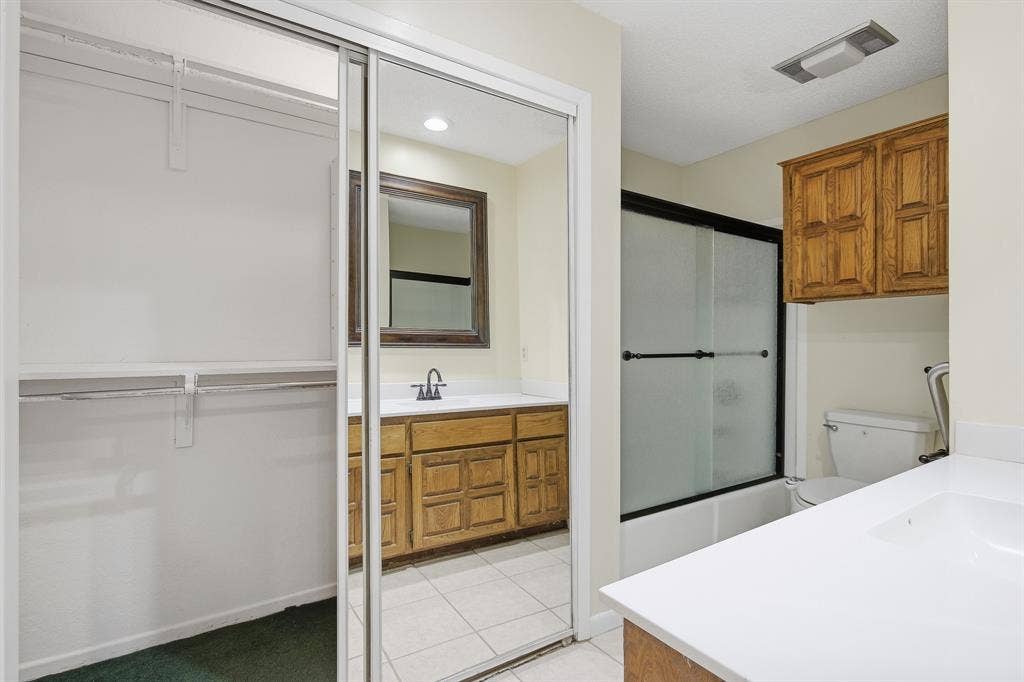 Mirrored sliding closet doors, built-in shelving, white tile flooring, wood-finish vanity with white countertop, and a shower-tub combination with sliding glass doors