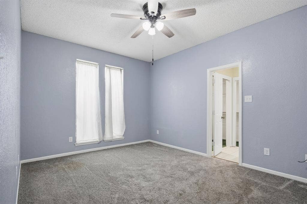 Gray carpeted room featuring two tall windows, a ceiling fan with integrated lighting, and a white paneled door