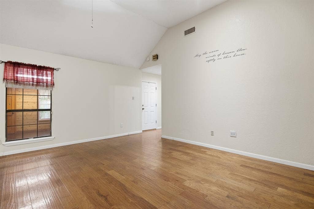 Vaulted ceiling, hardwood flooring, white paneled door, window with dark trim