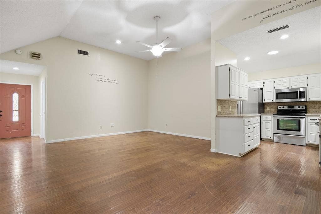 Vaulted ceiling with a ceiling fan, wood-finish flooring, recessed lighting, white kitchen cabinetry, and stainless steel appliances