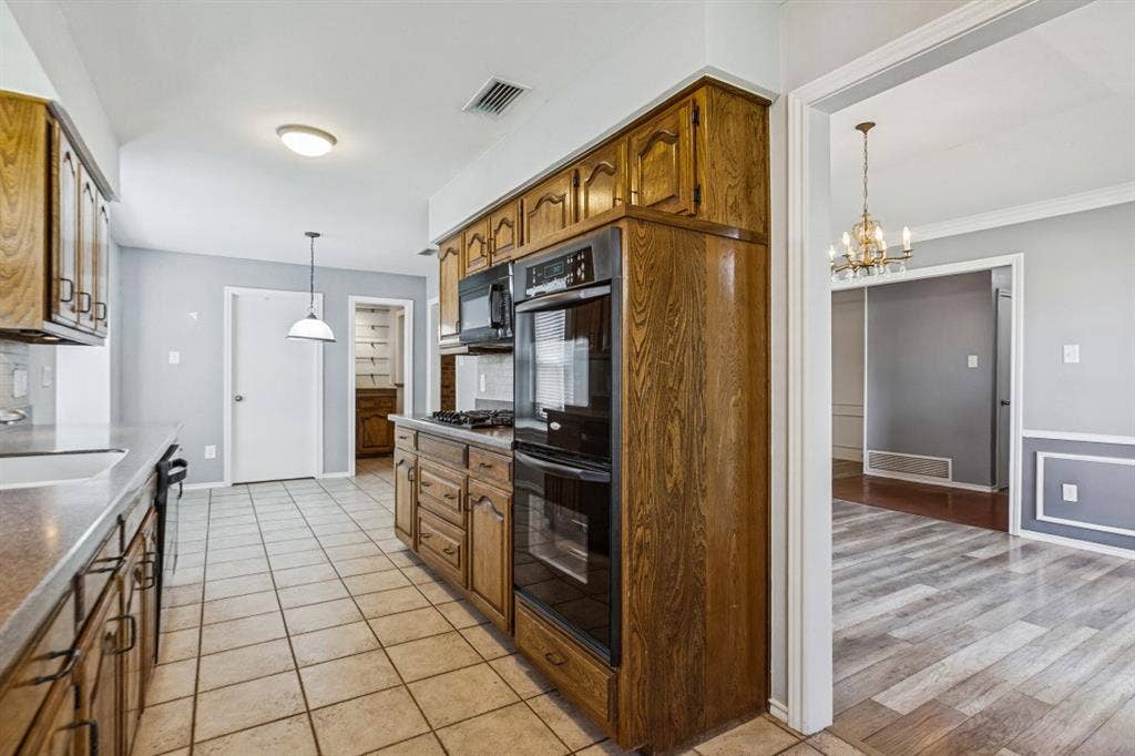 Spacious kitchen featuring rich wood cabinetry with raised-panel detailing, dual wall-mounted ovens, tile flooring, recessed lighting, and pendant fixtures
