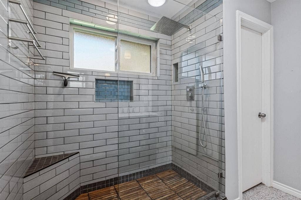 Glass-enclosed shower with subway tile surround, built-in bench, and wood-finish flooring