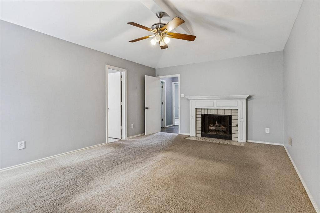 Vaulted ceiling with a ceiling fan, carpet flooring, and a fireplace featuring a white mantel and brick surround