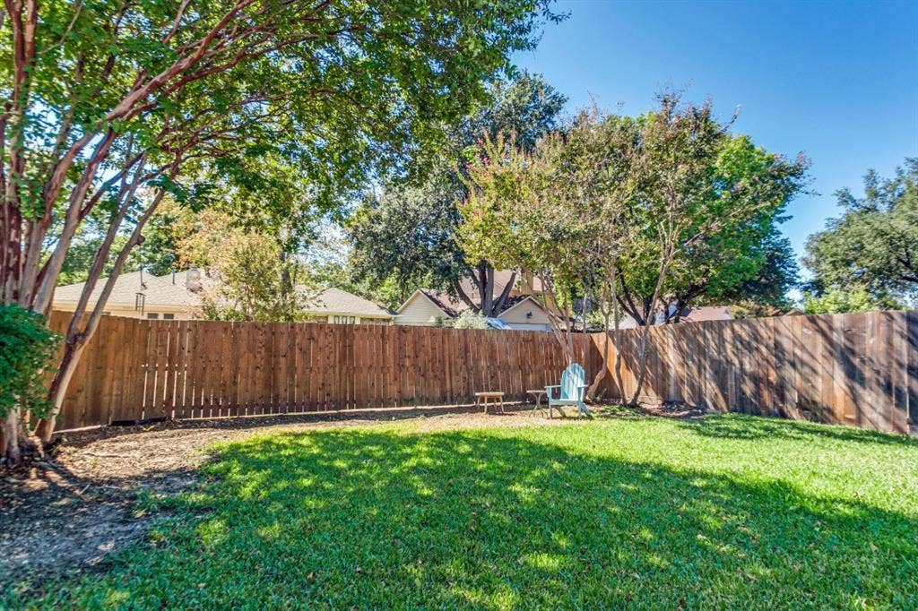 Expansive backyard featuring a manicured lawn, mature trees, and a privacy fence