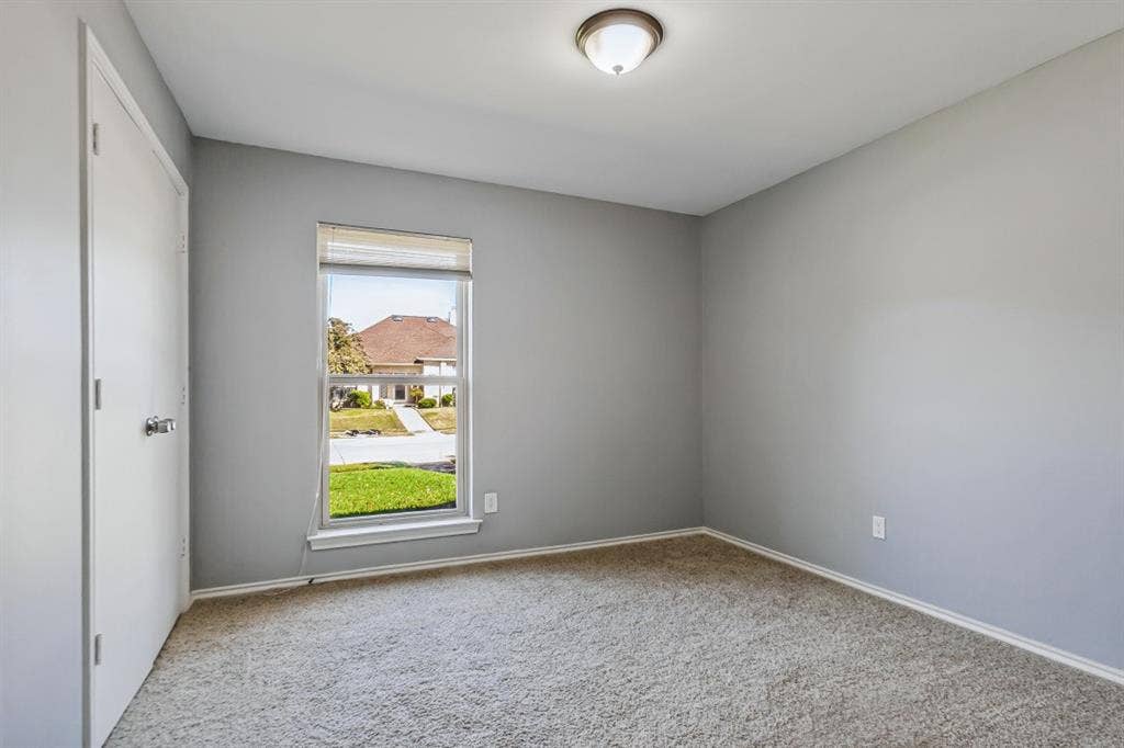 Light gray wall color, carpeted flooring, single window with blinds, flush-mount ceiling light, white trim throughout