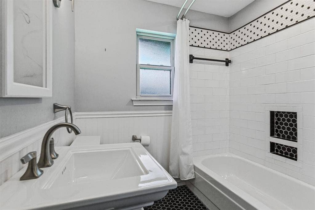 Pedestal sink with brushed nickel faucet, subway tile bath surround, black honeycomb tile flooring, and integrated shower niche