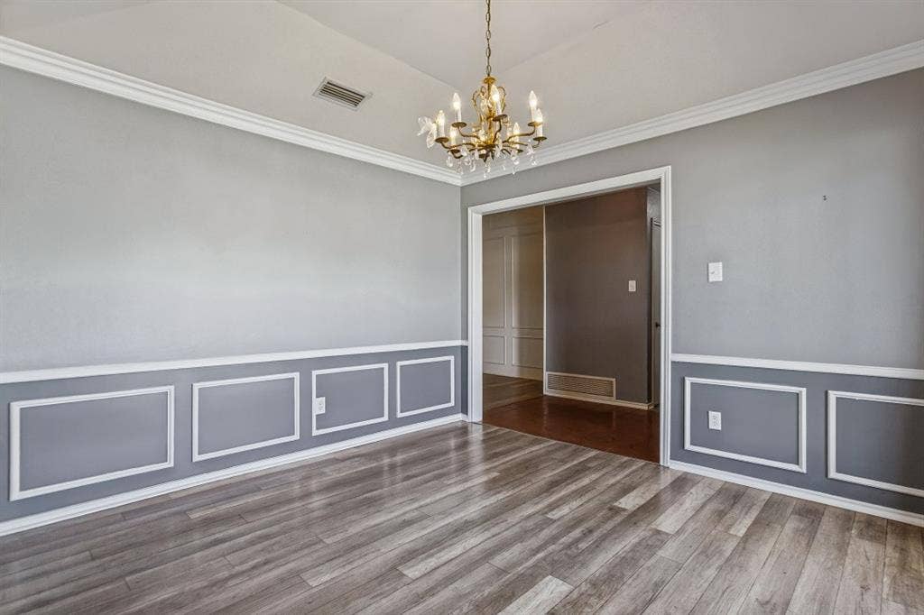 Wood-finish flooring, decorative wainscoting, crown molding, and a brass chandelier