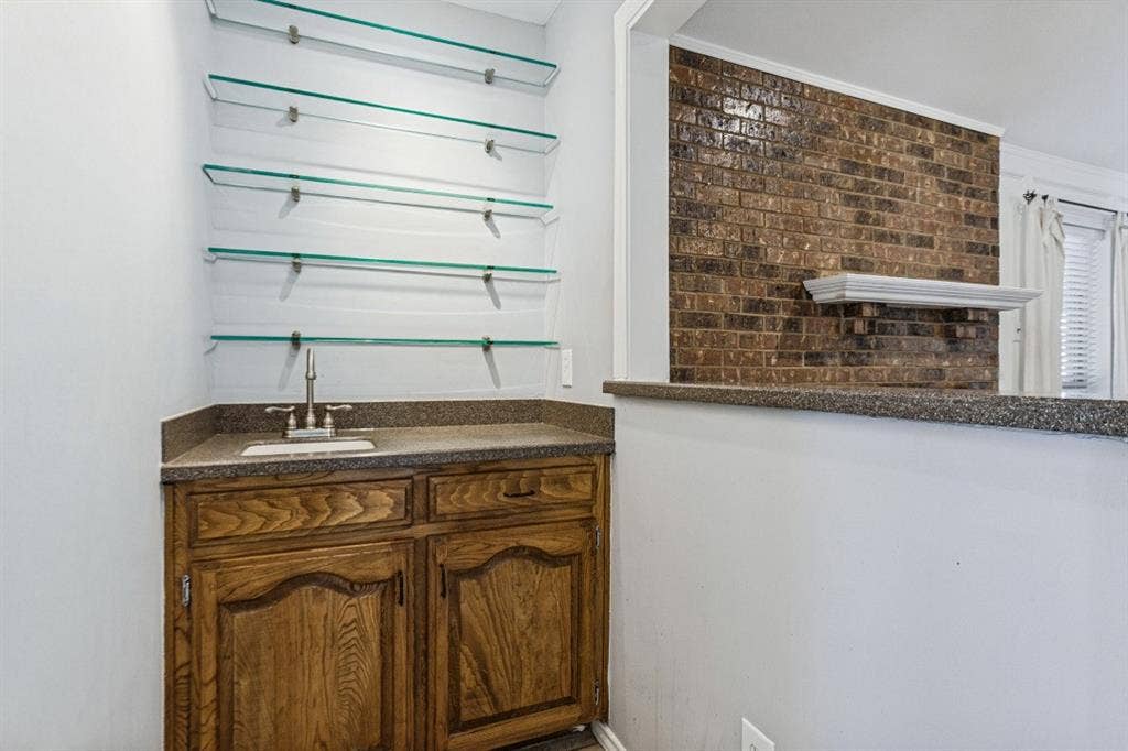 Built-in wet bar with wood cabinetry, granite-finish countertop, and a stainless steel sink