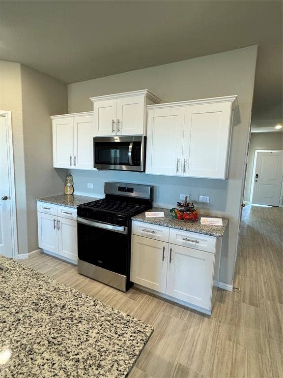Kitchen featuring stainless steel range, white cabinetry, light stone counters, and light wood-style flooring