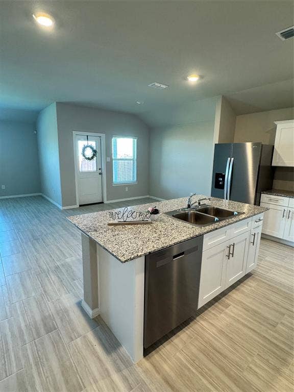 Kitchen with white cabinets, dishwasher, stainless steel fridge, a kitchen island with sink, and light wood-style floors