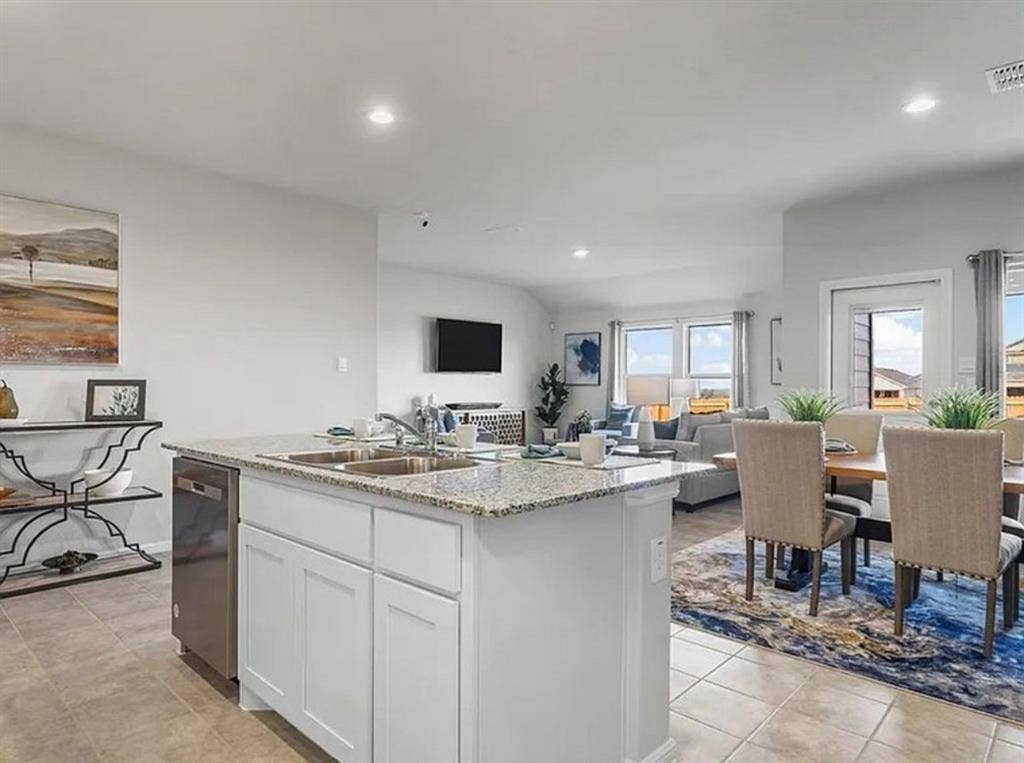 Kitchen featuring white cabinets, light stone countertops, a center island with sink, dishwasher, and recessed lighting