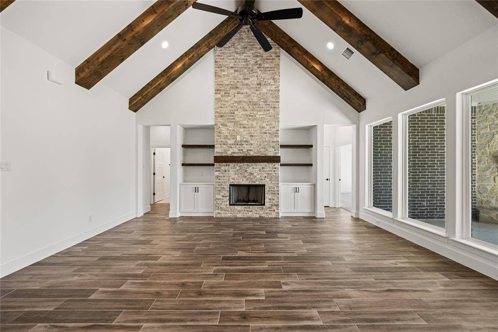 104 Oak Meadow Lane, Weatherford, TX 76085 Vaulted ceiling with exposed wood beams, brick fireplace with wood mantle, built-in shelving and cabinetry, wood-finish flooring, and multiple large windows