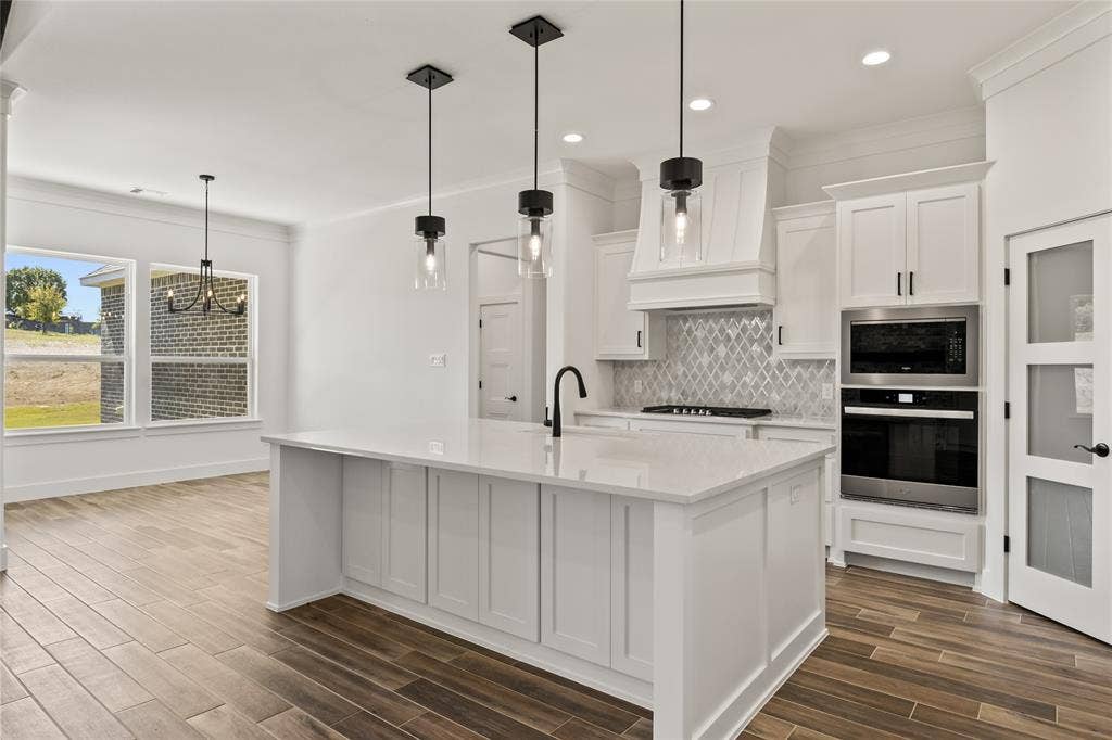 104 Oak Meadow Lane, Weatherford, TX 76085 White kitchen featuring an island with a light-colored countertop, built-in stainless steel appliances, and wood-finish flooring
