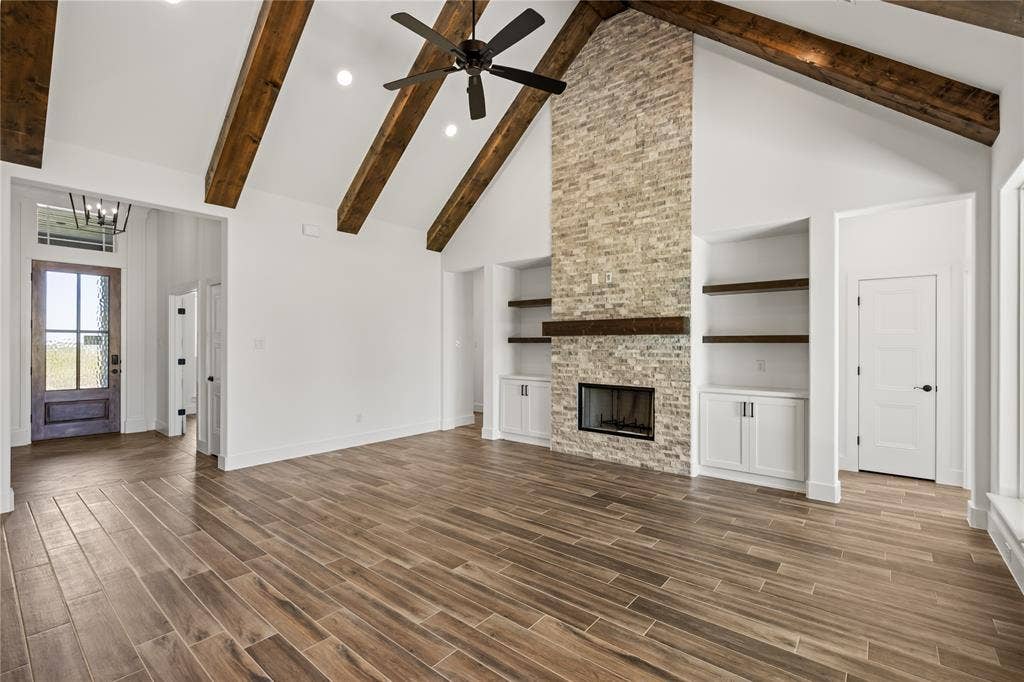 104 Oak Meadow Lane, Weatherford, TX 76085 Vaulted ceiling with exposed wood beams, wood-finish flooring, stone fireplace with a wood mantle, recessed lighting, and built-in cabinetry with open shelving