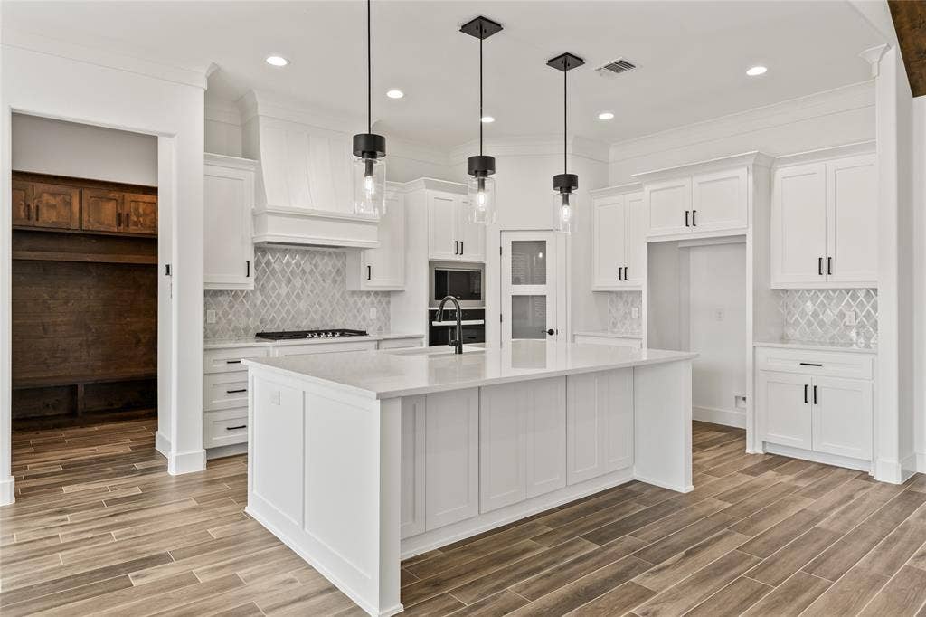 104 Oak Meadow Lane, Weatherford, TX 76085 Spacious kitchen featuring an expansive center island with countertop seating, white shaker cabinetry, patterned tile backsplash, and wood-finish flooring