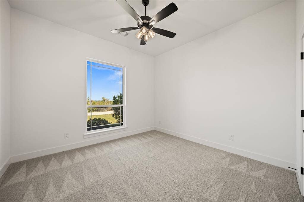 104 Oak Meadow Lane, Weatherford, TX 76085 Bright room featuring a ceiling fan with integrated lighting, a large window, white walls, and patterned carpet flooring
