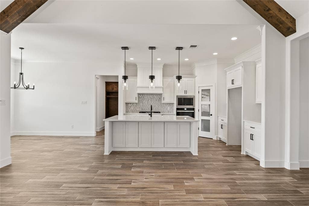 104 Oak Meadow Lane, Weatherford, TX 76085 Spacious kitchen featuring an island with three pendant lights, white cabinetry, integrated oven, and a patterned tile backsplash