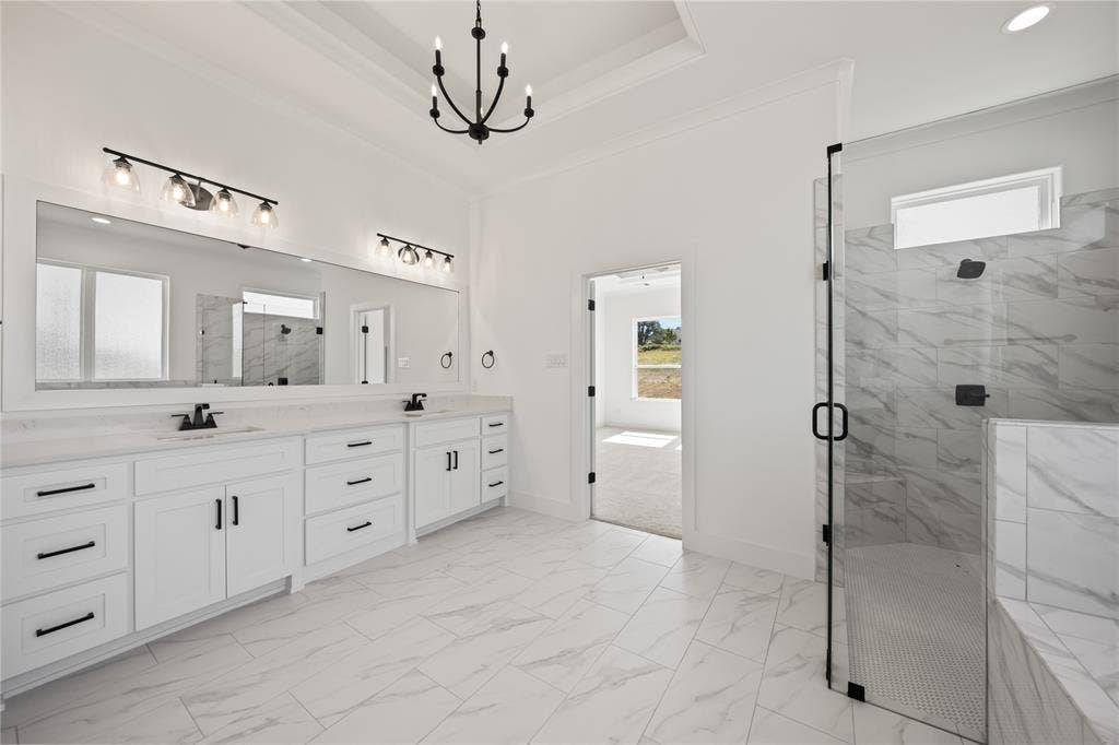 104 Oak Meadow Lane, Weatherford, TX 76085 Dual vanity with white cabinetry and dark hardware, large framed mirror, walk-in shower with glass enclosure, white tile flooring, and tray ceiling
