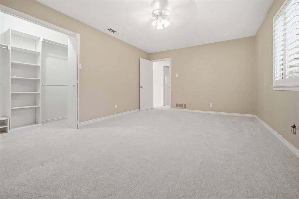 Wall-to-wall carpeting, window with plantation shutters, ceiling fan with light fixture, and built-in closet shelving