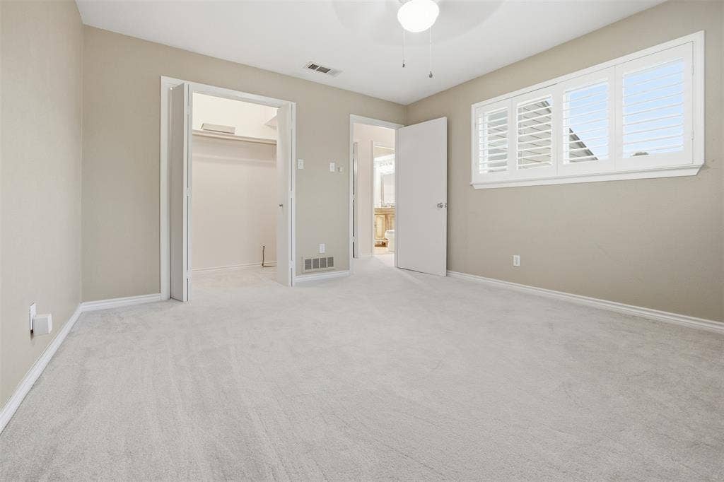 Light neutral wall color, plush light-toned carpeting, window with plantation shutters, ceiling fan with integrated lighting, and built-in closet shelving