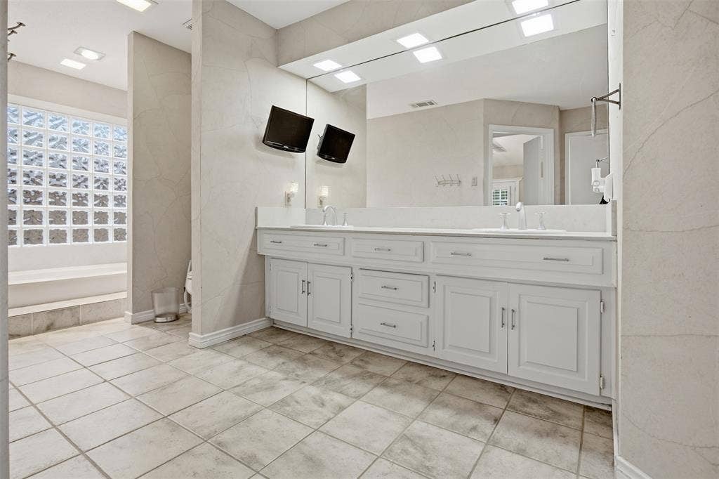 Dual vanity with white cabinetry, integrated sinks, an expansive mirror, and tile flooring