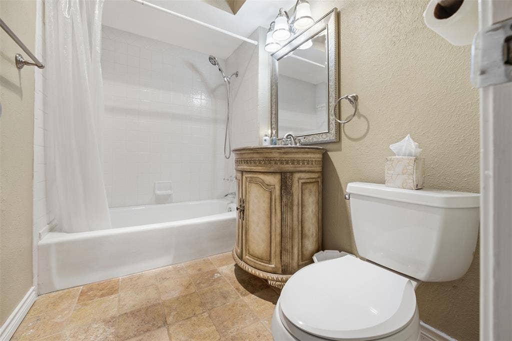 Neutral-toned tile flooring, bathtub with white subway tile surround, vanity with decorative wood-finish cabinetry, framed mirror, and chrome vanity lighting