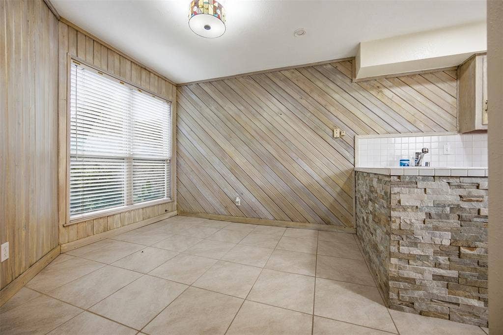 Tile flooring, paneled walls, large window, stone-clad counter base, and tiled backsplash