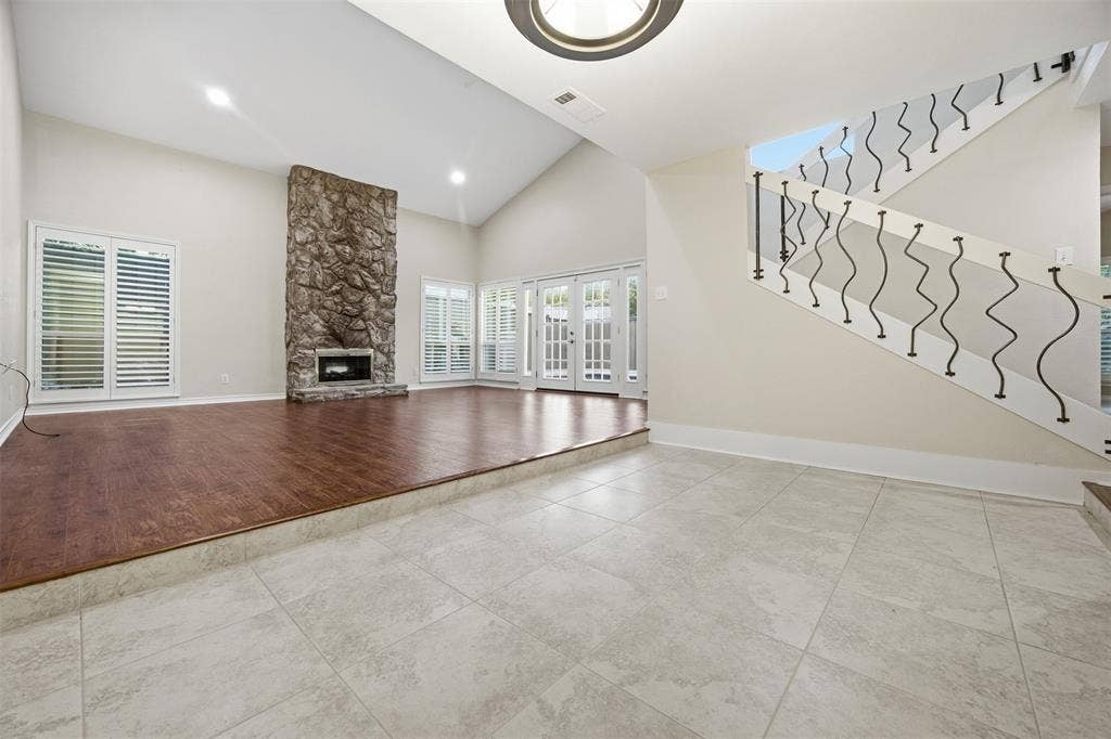Vaulted ceilings, a stone-clad fireplace, wood-finish flooring, white plantation shutters, and a staircase with decorative wrought iron balusters