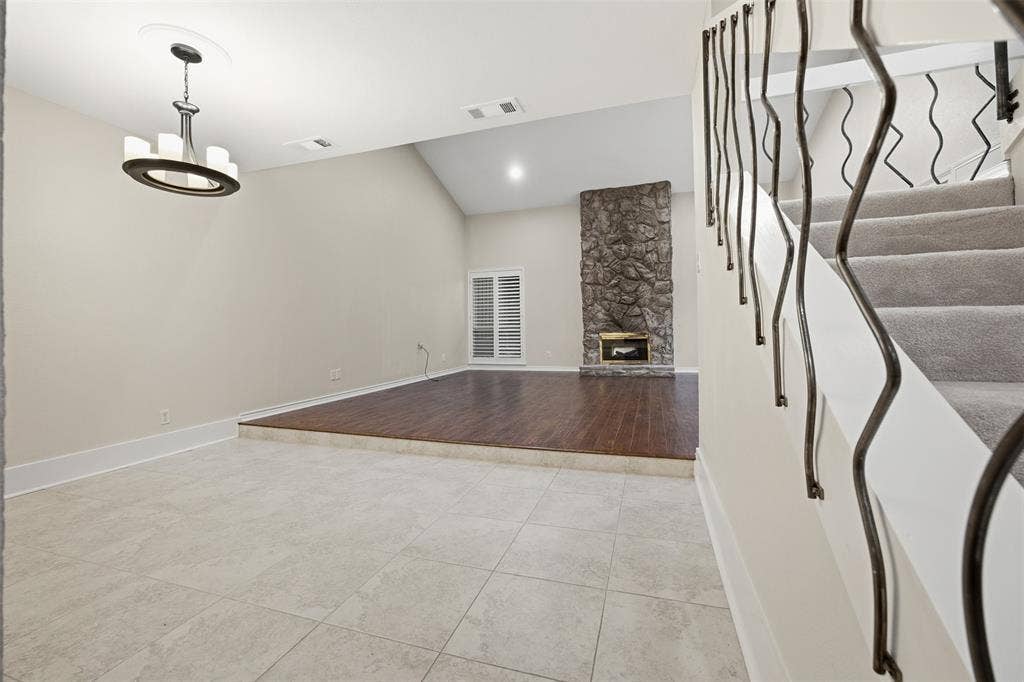 Two-story interior with varied flooring, a vaulted ceiling, and a stone fireplace