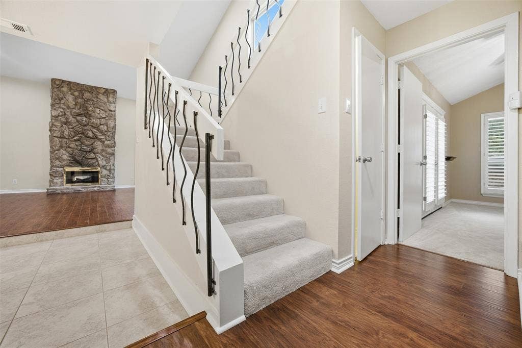 Carpeted staircase with decorative iron railings, tile flooring, wood-finish flooring, and a stone-clad fireplace