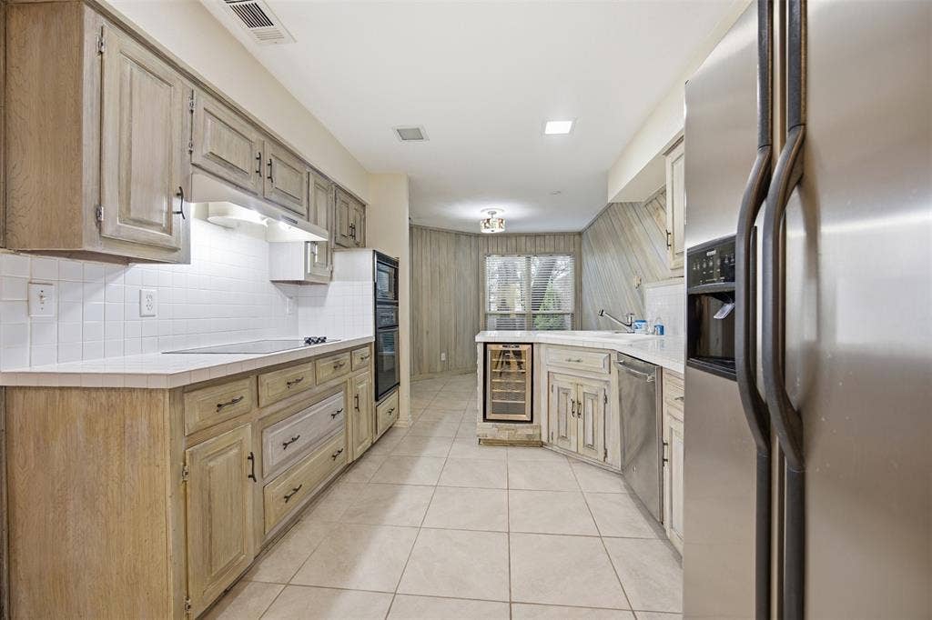 Kitchen featuring light wood-finish cabinetry, white countertops, a tiled backsplash, and stainless steel appliances