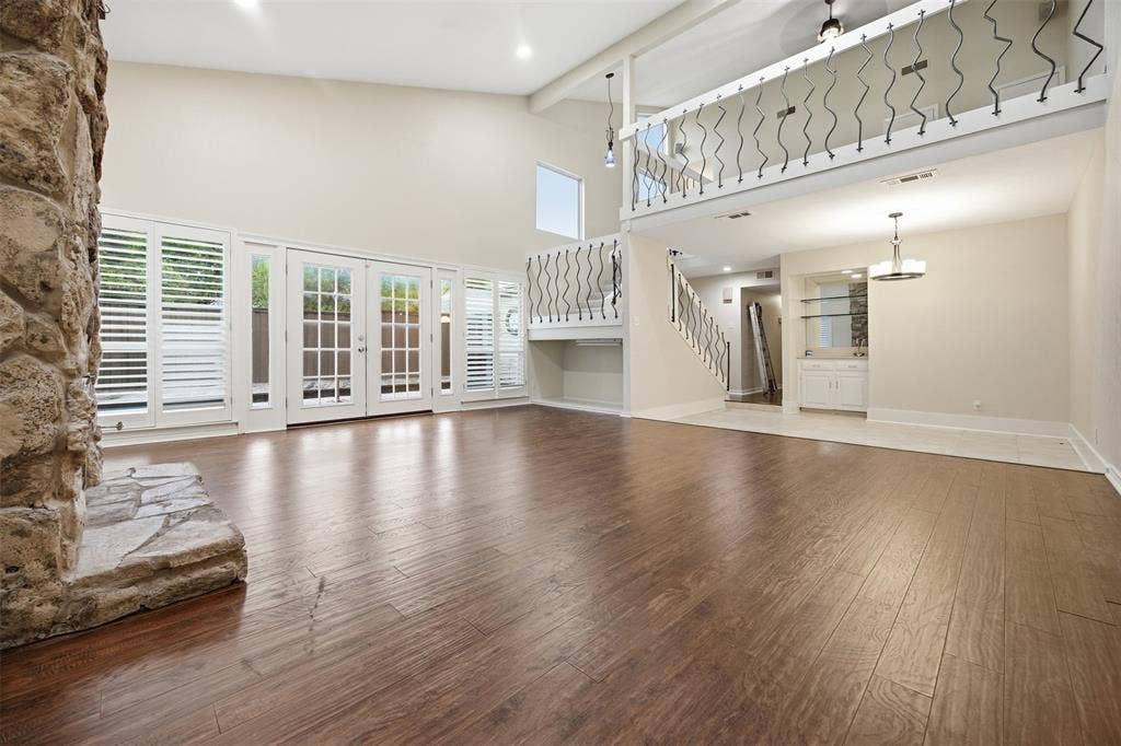 Spacious living area featuring wood-finish flooring, a stone-clad fireplace, and multiple French doors with plantation shutters