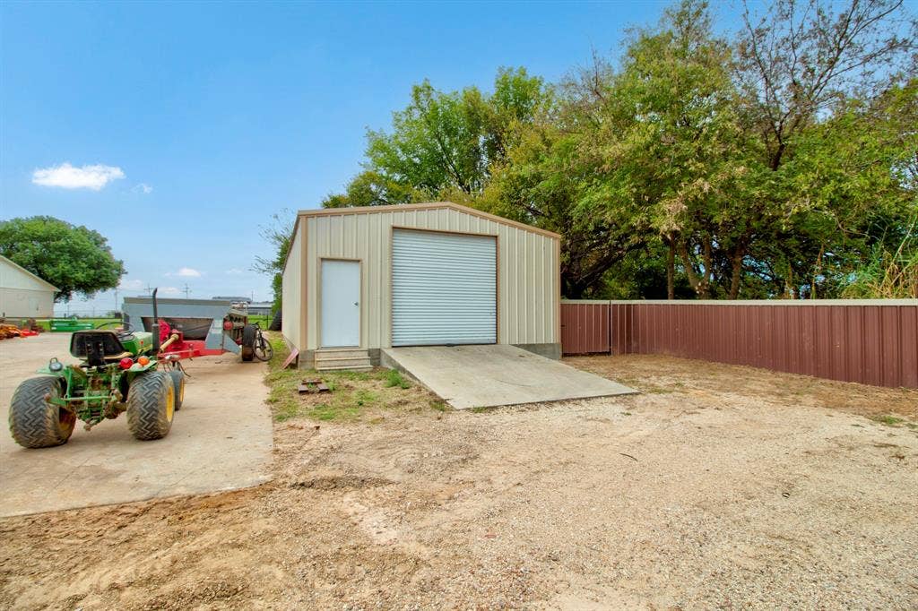 Detached metal workshop featuring a roll-up bay door, personnel entry door, and concrete ramp