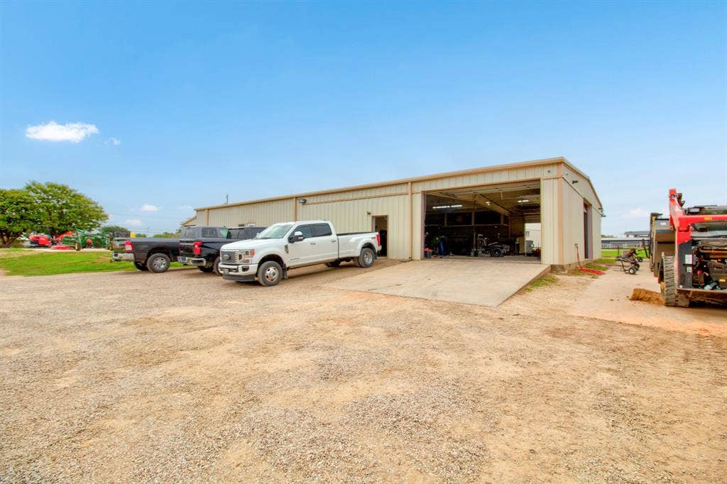 Metal-siding workshop featuring an open-bay entrance, concrete approach ramp, and expansive gravel parking area