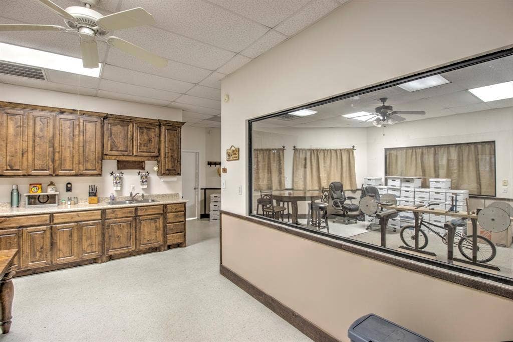 Stained wood cabinetry, stone-finish countertops, dual-basin stainless steel sink, large interior glass partition, and drop ceiling with recessed lighting