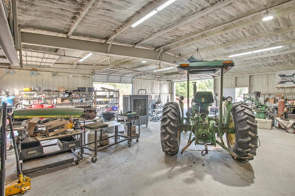 Spacious workshop featuring a concrete floor, metal-paneled walls, exposed ceiling framing, and overhead fluorescent lighting