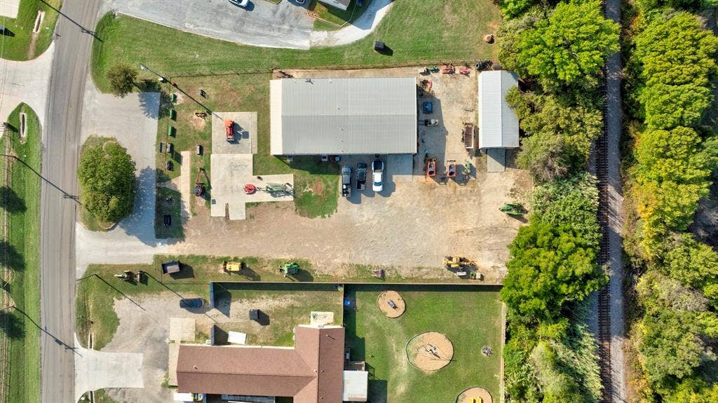 Aerial perspective of the property featuring a metal-sided workshop, a detached storage building, a paved surface, and expansive gravel lot space