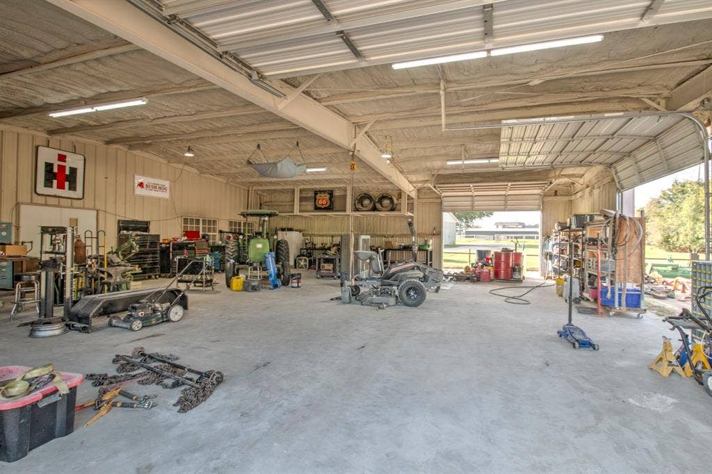 Expansive workshop featuring concrete flooring, exposed steel beams, high-clearance overhead door, and industrial-style interior lighting
