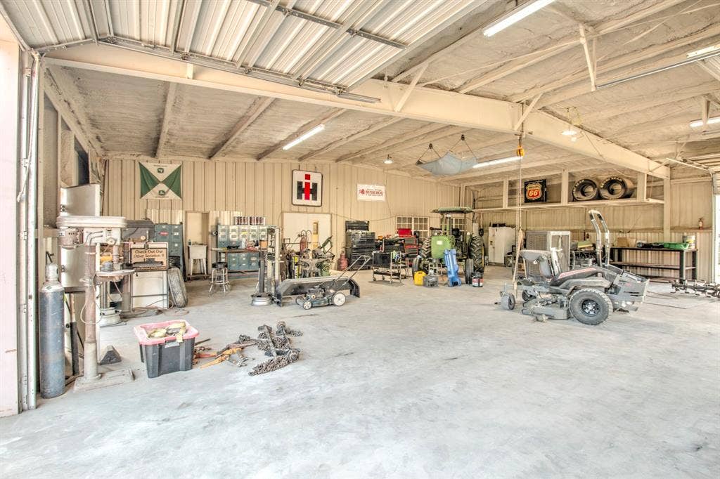 Spacious workshop featuring a concrete floor, high-clearance overhead garage door, built-in elevated storage shelving, and integrated linear overhead lighting